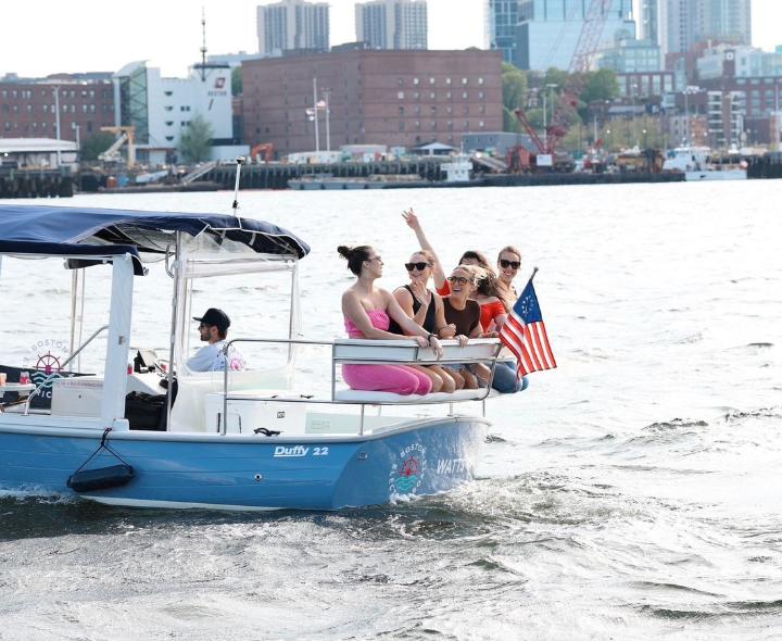A happy group of women smiling and waving their hands while on their private party boat rental in Boston Harbor